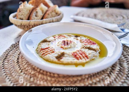 Gros plan de houmous garni de paprika et d'huile d'olive, servi avec du pain sur un napperon tissé dans un restaurant. Banque D'Images