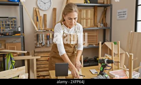 Femme concentrée mesurant du bois dans un atelier de menuiserie bien équipé. Banque D'Images