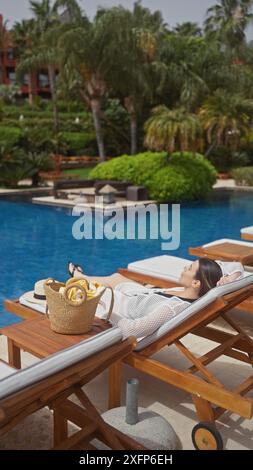 Une femme détendue profitant du cadre extérieur tranquille d'un complexe hôtelier au bord de la piscine à bali, se prélassant sur un transat pendant ses vacances. Banque D'Images