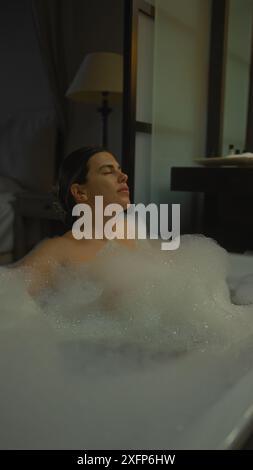 Femme hispanique détendue profitant d'un bain moussant dans une chambre d'hôtel, rayonnant de luxe et de sérénité. Banque D'Images