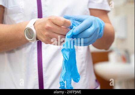 Gros plan d'une infirmière mettant des gants en latex bleu sur un fond clinique. Photo de haute qualité Banque D'Images