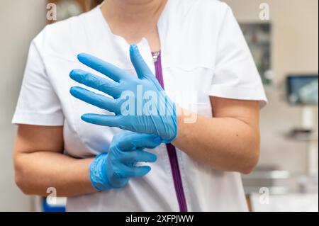 Gros plan d'une infirmière mettant des gants en latex bleu sur un fond clinique. Photo de haute qualité Banque D'Images