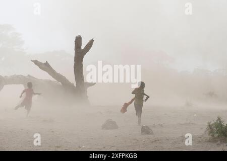 Enfants Massaï courant dans un tourbillon de poussière et de sable. Parc national d'Amboseli, Kenya. Août 2017. Banque D'Images