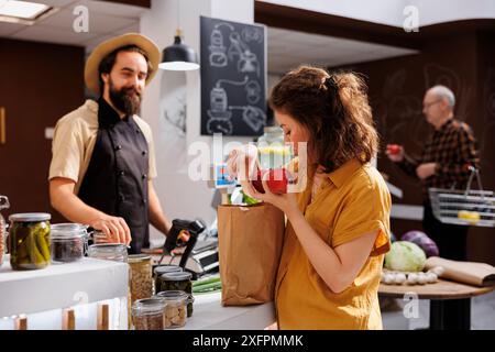 Femme à la caisse de magasin zéro déchet payant pour des légumes sans produits chimiques. Client dans une épicerie locale sans plastique utilisant un sac en papier décomposable pour réduire l'impact environnemental Banque D'Images