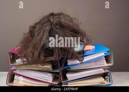Femme fatiguée épuisée dormant sur une pile de dossiers, burnout, stress et surmenée, pression au travail Banque D'Images