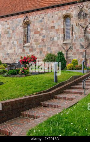 Jardin devant une église avec mur de pierre coloré, tuiles rouges et fleurs bien entretenues, wangerland, basse-saxe, allemagne Banque D'Images