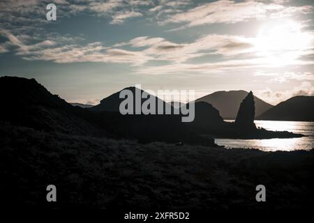 Une vue imprenable sur le coucher du soleil dans les îles Galapagos, avec des formations volcaniques silhouettes et Pinnacle Rock contre un ciel coloré et un océan serein. Banque D'Images