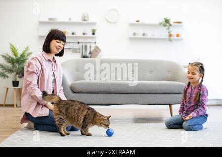 Mère et fille jouant avec le chat dans le salon confortable Banque D'Images