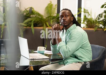 Travaillant à la maison, homme assis au bureau avec ordinateur portable et tasse à café Banque D'Images