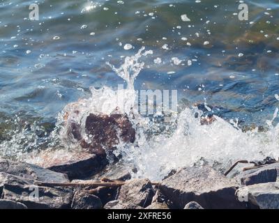 Vague d'eau qui s'écrase contre un gros rocher au bord d'un lac. journée d'été lumineuse. soleil éclatant. Banque D'Images