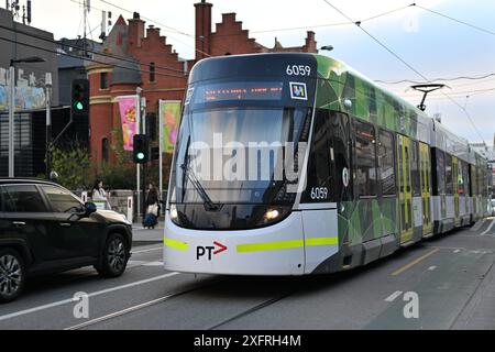 Tramway de classe E, avec livrée PTV et logo, passant au-dessus du passage piétonnier à l'extérieur de la gare de South Yarra en fin d'après-midi Banque D'Images