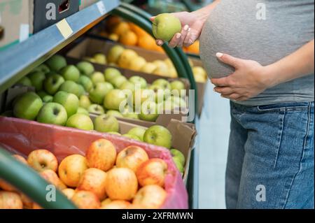 La femme enceinte choisit des pommes dans le magasin. Banque D'Images