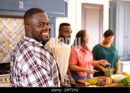 Homme souriant dans la cuisine avec divers amis préparant la nourriture et profitant du temps ensemble Banque D'Images