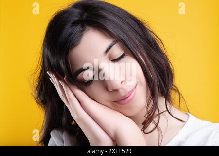 Jeune femme aux longs cheveux foncés dort paisiblement, les mains sur le visage, exsudant calme et sérénité dans un cadre élégant. Ses yeux fermés montrent contentement et Banque D'Images