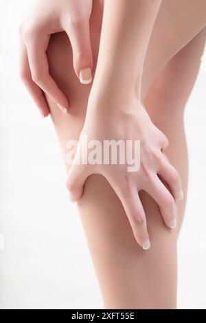 Femme en douleur tient sa jambe, soulignant l'importance de chercher de l'aide médicale pour l'inconfort des jambes. Douleurs aux jambes, crampes, santé, blessures, bien-être Banque D'Images