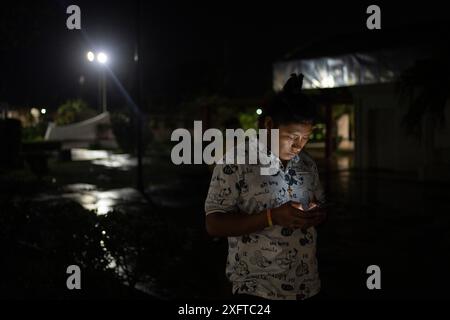 Tulum, Mexique. 04 juillet 2024. Un homme utilise son téléphone dans un refuge d'urgence où il réside pour se protéger des effets de l'ouragan Beryl. Crédit : Felix Marquez/dpa/Alamy Live News Banque D'Images