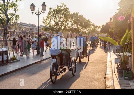 Hoi an (Hoian), Vietnam - 11 avril 2018 : touristes marchant le long de la digue de la rivière Thu bon et poussant à vélo (trishaws) dans la ville antique de Hoi an Banque D'Images