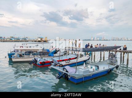 Penang Island, Malaisie-avril 25 2023 : le long de l'ancienne jetée promenades en bois, près du coucher du soleil, les visiteurs se tiennent debout, assis et prendre des photos au bord de l'eau, avec un petit moteur Banque D'Images