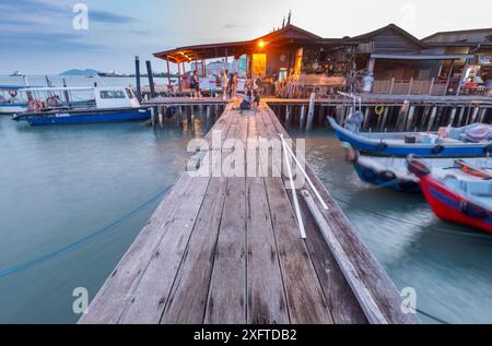 Penang Island, Malaisie-avril 25 2023 : le long de l'ancienne jetée promenades en bois, près du coucher du soleil, les visiteurs se tiennent debout, assis et prendre des photos au bord de l'eau, avec un petit moteur Banque D'Images