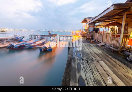 Penang Island, Malaisie-avril 25 2023 : le long de l'ancienne jetée promenades en bois, près du coucher du soleil, les visiteurs se tiennent debout, assis et prendre des photos au bord de l'eau, avec un petit moteur Banque D'Images