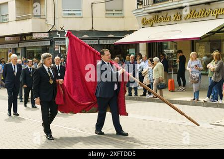 Astorga, Espagne - 4 juin 2023 : un homme porte un grand drapeau rouge alors qu'il marche en procession dans les rues d'Astorga, Espagne. D'autres personnes regardent an Banque D'Images