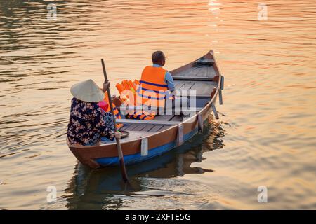 Touriste voyageant en bateau au coucher du soleil, Hoi an Ancient Town (Hoian), Vietnam. Femme vietnamienne dans le chapeau traditionnel en bambou ramant sur la rivière Thu bon Banque D'Images
