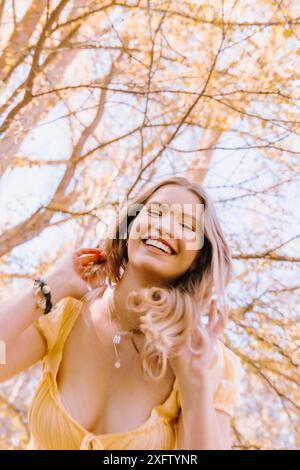Femme dans une robe jaune souriant joyeusement sous les arbres en fleurs Banque D'Images