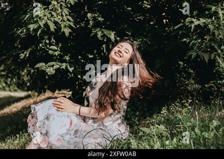 Une belle femme est assise sur l'herbe et profite du soleil Banque D'Images