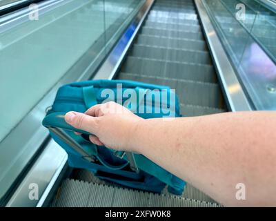 Main et bras tirant la valise sarcelle sur un escalier roulant à l'aéroport CVG Banque D'Images