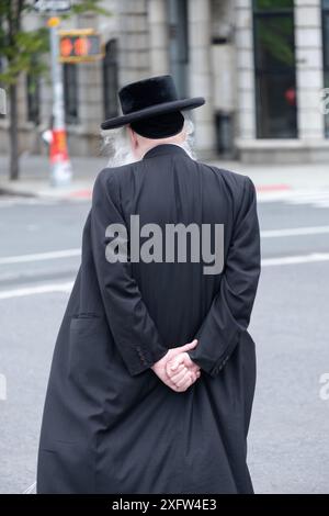 Un homme juif orthodoxe anonyme marchant les mains ensemble derrière son dos. Sur Lee Avenue à Williamsburg, Brooklyn, New York, 2024. Banque D'Images