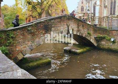 30-10-2014 Bruges, Belgique - les touristes traversent un pont pittoresque en pierre et briques sur un canal de Bruges Banque D'Images