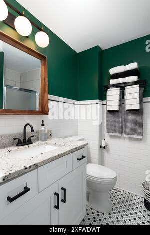 Une salle de bains avec des murs verts et des murs de carreaux de métro blancs, un miroir encadré en bois et un comptoir de quartz sur un meuble de toilette blanc. Banque D'Images