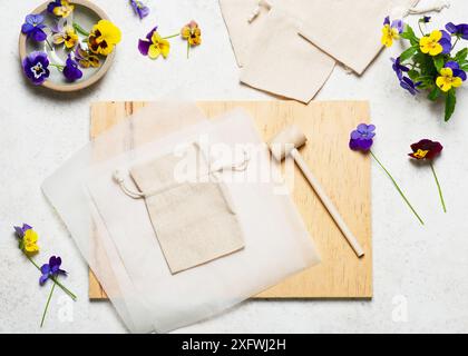 Vue de dessus du lieu de travail avec sacs en tissu, fleurs de pensées, marteau en bois, papiers transparents, bloc de bois. Étape par étape de la création d'un sac en coton Banque D'Images