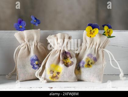 Trois petits sacs en tissu faits à la main avec de belles impressions de fleurs de pensées martelées sur l'étagère de cuisine blanche. Matériau naturel artisanal pour concept d'enfants. Banque D'Images