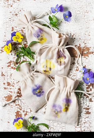 Vue de dessus des petits sacs en tissu faits à la main avec de belles impressions de fleurs de pensées martelées sur une table en bois vintage. Matériel naturel artisanal pour les enfants Concepp Banque D'Images