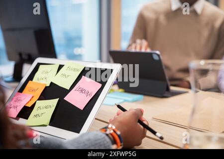 Image recadrée de femme d'affaires prenant des notes avec un collègue tout en utilisant un ordinateur portable dans le bureau Banque D'Images