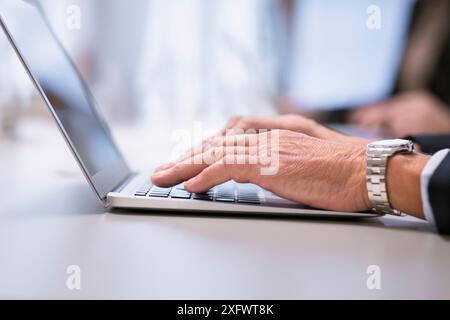 Image recadrée de l'homme d'affaires senior utilisant l'ordinateur portable à la table dans le bureau Banque D'Images