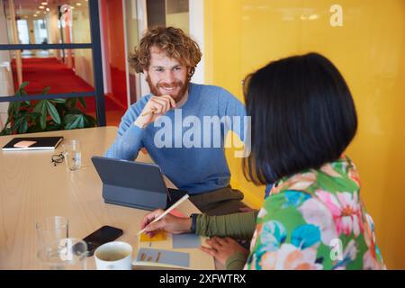Homme d'affaires souriant regardant une collègue féminine tout en étant assis dans le bureau Banque D'Images
