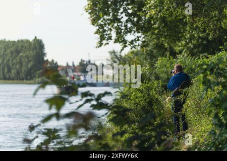 Speyer, Allemagne. 5 juillet 2024. Homme avec caméra debout dans les buissons, prenant des photos du sous-marin arrivant. Le transport final du sous-marin U17 du Technik Museum Speyer au Technik Museum Sinsheim se déroule sur un mois entier, à partir du 30 juin. Pendant ce temps, le sous-marin lourd de 500 tonnes sera transporté sur les routes et les rivières. Pour surmonter divers obstacles comme les ponts bas ou les lignes de chemin de fer, le sous-marin désaffecté sera incliné à un angle de 73 degrés. Crédit : Gustav Zygmund/Alamy News Banque D'Images