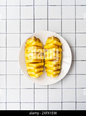 Vue de dessus de deux moitiés d'ananas magnifiquement tranchées sur une plaque blanche, placée sur une surface carrelée. Pose à plat. Copier l'espace Banque D'Images