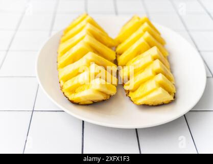 Deux moitiés d'ananas magnifiquement tranchées sur une assiette blanche, placées sur une surface carrelée. Pose à plat Banque D'Images