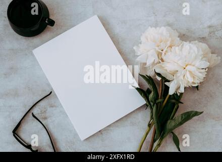 Bouquet de fleurs de pivoine blanche, maquette vide blanche de couverture de magazine, tasse de thé et lunettes noires sur table grise. Vue de dessus. Copier l'espace. Plat la Banque D'Images