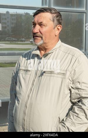 Un homme attrayant, jeune, aux cheveux gris de 70 ans avec pour toile de fond des immeubles de bureaux en verre miroir. Portrait d'une personne âgée aux cheveux gris M. Banque D'Images