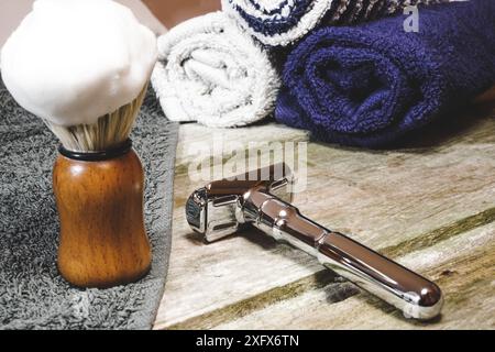 Gros plan horizontal d'un rasoir de sécurité brillant avec une brosse à raser en mousse et des serviettes de barbier. Fournitures de rasage humide dans la table en bois. Banque D'Images