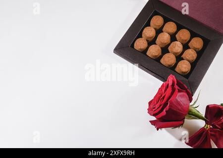 Une boîte de chocolats et une rose rouge sont élégamment exposées sur une surface blanche, créant une scène charmante et romantique Banque D'Images