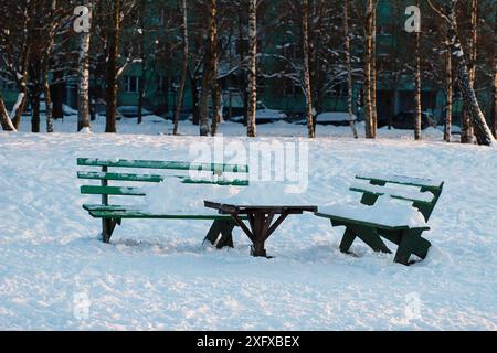 Deux bancs en bois vert et une table dans une cour de ville, dans la neige. Banque D'Images