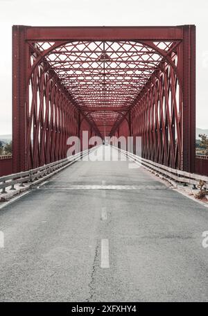 Un pont en treillis rouge avec une route passant sous lui, présentant une symétrie et un design rectangulaire. Le pont est en métal et comprend une passerelle pour Banque D'Images