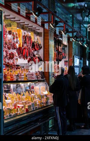 Séville, Espagne. 5 février 2024 - les acheteurs parcourent les viandes séchées et les fromages au Mercado de Triana. Banque D'Images