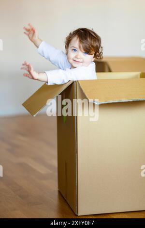 Cute baby girl sitting sourire tout-petit à l'intérieur de boîte en carton brun. Banque D'Images