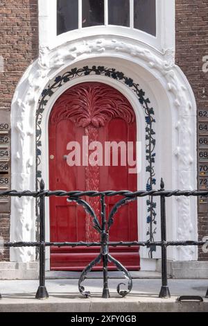 Une porte rouge avec une porte en fer noir devant elle. La porte est décorée de vignes Banque D'Images